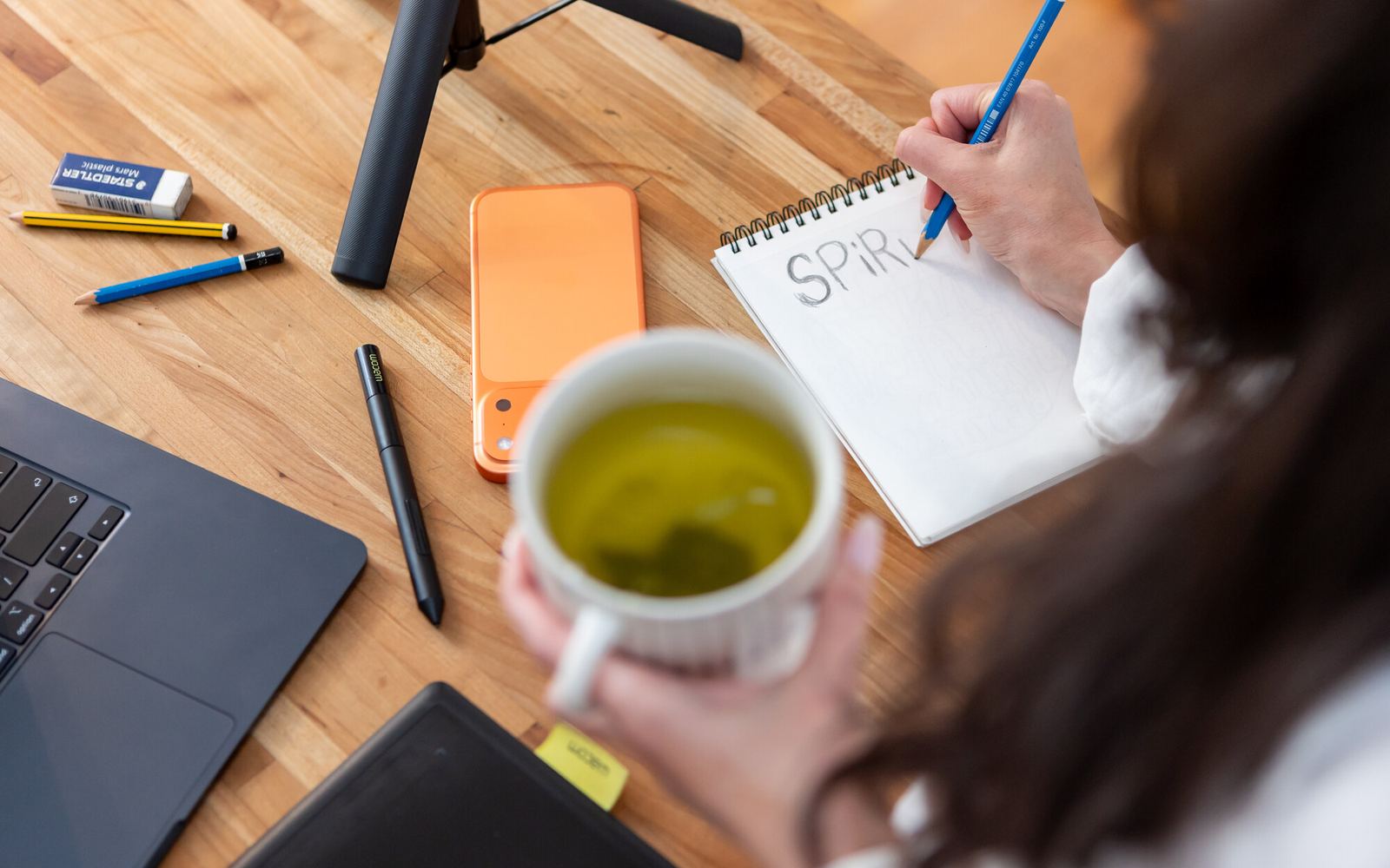 Overhead view of a desk with notebook, laptop and tea